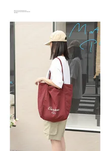 Side view detail of a woman carrying a burgundy nylon tote bag with white letter print