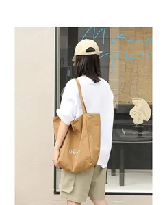 Detailed lifestyle view showing a camel nylon tote bag with white lettering worn by a model
