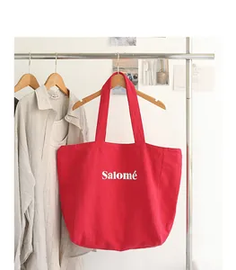 Red linen tote bag with white Salomé print hanging on a clothing rack in a cozy room