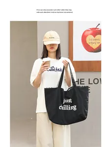Woman holding a black nylon tote bag with just chilling print in a casual outdoor setting