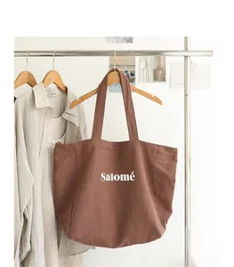 Brown linen tote bag with white Salomé letter print hanging on a clothing rack detail