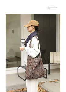 Détail d'un sac en toile marron avec broderie paisley blanche porté par un mannequin.