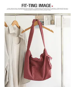 Close-up of a burgundy checkered messenger bag with knotted shoulder strap detail.