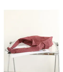 Red checkered messenger bag with unique knot strap detail on minimalist acrylic table