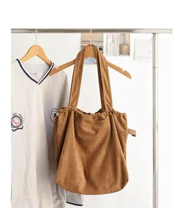 Close-up of a brown suede drawstring tote bag with pleated detail on a wooden hanger