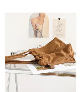 Detail of brown faux suede tote bag with drawstring pleats in a modern aesthetic setting.