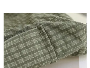 Close-up detail of green checkered nylon fabric with reinforced stitching on a messenger bag