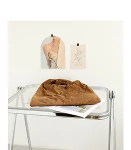 Brown suede drawstring shoulder bag with elegant pleated detail displayed on a minimalist glass table