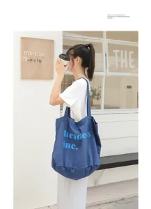 Bolso tote de lona lavada azul con estampado de letras en el hombro de una modelo