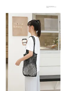 Model carrying a black hand-woven mesh shoulder bag in a cafe setting