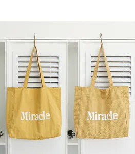 Vista detallada de dos bolsos tote amarillos con estampado Miracle blanco en taquillas blancas