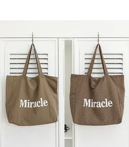 Detalle de los bolsos tote caqui y a cuadros con el estampado de letras Miracle blanco