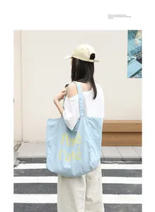 Stylish light blue nylon tote bag with yellow Pepé t'uté text print on a fashion model