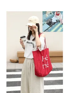 Red nylon tote bag with white lettering shown in a stylish street setting