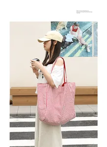 Female model carrying a red and white vertical striped nylon tote bag on a sunny city street