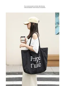 Street style view of a black nylon tote bag with white letter print and striped lining