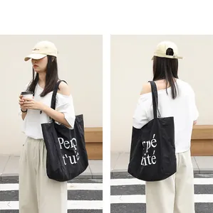 Detail view of a black nylon tote bag featuring a white letter print on a casual model.