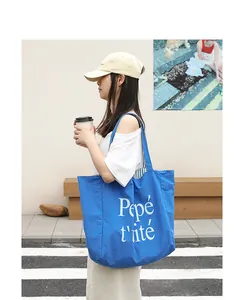 Detailed view of the vibrant blue nylon tote bag with white letter print and model