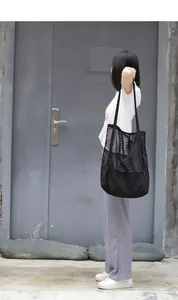 Bolso tote de malla negra con fondo de lona llevado al hombro en un entorno urbano