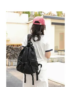 Back view of casual black nylon drawstring backpack worn by a model in an outdoor setting.