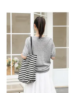 Back view of a model carrying a stylish black and white striped canvas tote bag outdoors.