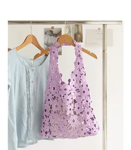 Detail of purple floral crochet hollow-out shoulder bag hanging on a wooden hanger.