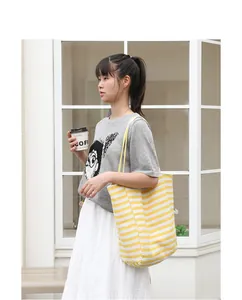 Casual yellow and white striped canvas tote bag worn by a model in a street setting.