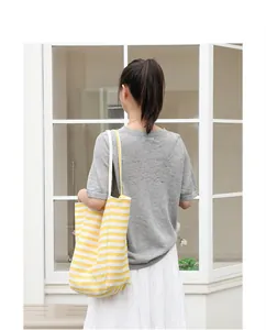 Back view of a model wearing a yellow and white striped canvas tote bag in leisure style.