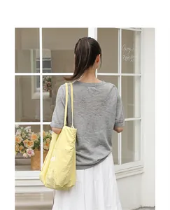 Bolso tote casual de lona amarilla con estampado de letras visto por detrás en hombro