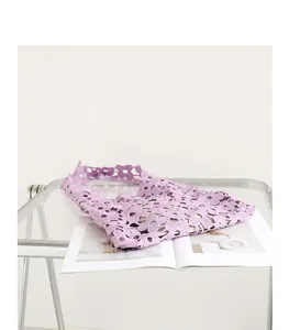 Macro view of a purple hollowed-out lace flower shoulder bag on a minimalist glass table.
