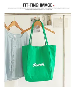 Bolso tote verde con estampado Beach colgado en un perchero de estudio.