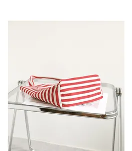 Detail view of the bottom of a red and white striped canvas tote bag on a glass cart.