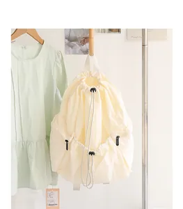 Detail view of a cream drawstring nylon backpack with side zippers and cord lock.
