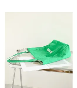 Vista detallada de un bolso de nailon verde vibrante con letras blancas en mesa transparente.