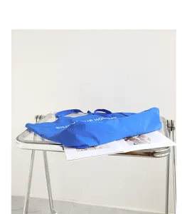 Blaue Nylon-Einkaufstasche mit weißem Holiday-Print auf einem klaren Acrylstuhl