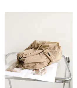 Detail view of a khaki crinkled nylon drawstring backpack on a glass table.