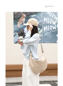 Primer plano de un bolso de media luna minimalista de cuero PU beige en un entorno urbano.