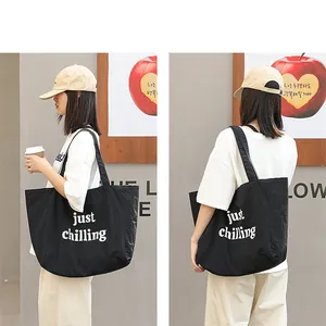 Casual black nylon tote bag with 'just chilling' text print shown on an Asian model