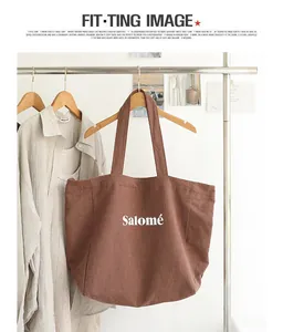 Brown linen tote bag with 'Salomé' print hanging on a clothing rack.