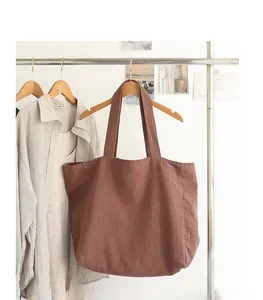 Detailed view of a brown linen tote bag hanging on a minimalist wooden hanger and rack