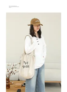 Vista detallada de un bolso de lona de lino beige con estampado Petit y cordón llevado por modelo
