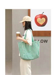 Detail view of a large green and white striped canvas tote bag carried by a model.