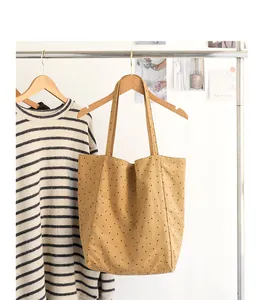 Detail view: Khaki canvas tote bag with black polka dot pattern hanging on garment rack