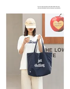 Casual lifestyle shot of a large navy blue nylon tote bag with 'just chilling' text print