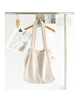 Vista detallada de un bolso tote de algodón y lino beige con cordón colgado en un perchero