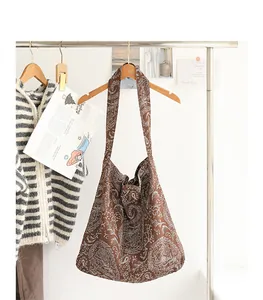 Gros plan détaillé du motif brodé blanc vintage sur un sac hobo en toile marron.
