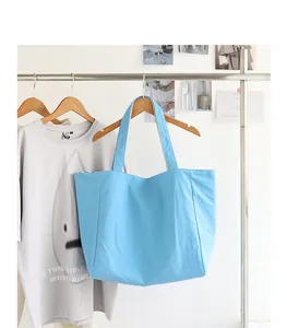 Minimalist light blue nylon tote bag hanging on a wooden hanger against a white wall.