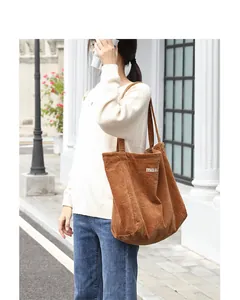 Detalle de un bolso tote de pana marrón con letras bordadas llevado por una modelo