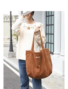 Bolso de pana marrón con bordado maaaaa llevado por una modelo en estilo informal.