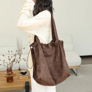 Stylish brown suede drawstring tote bag with pleated detail worn by model in a cozy room